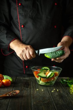 Şef mutfakta sebze salatası hazırlıyor. Bıçaklı vitamin salatası için taze salatalık dilimliyorum..
