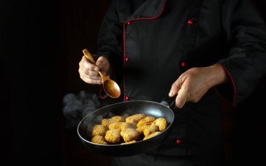 Aşçı kızartma tavasında çıtır çıtır nagit hazırlar. Karanlık bir arka planda lezzetli yemek ve yemekler için tarif. Boş reklam alanı.