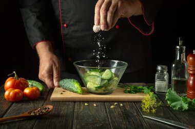 Şefin elleriyle sebze salatası pişirmek. Salatalık ve domates salatasına tuz ekliyorum..