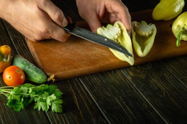 Mutfak masasını dilimlemeden önce şefin elinden olgun dolmalık biber soymak. Sebze leçesi pişirme konsepti.