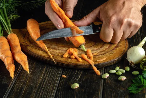 Peeling carrots for a vegetable dish by the hands of a cook on a cutting kitchen board. The concept of cooking a vegetarian diet