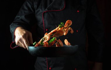 Aşçı tavada sebzeli karides kızartıyor. Hareket halinde donmak ya da havada uçmak. Koyu bir arka planda deniz ürünleriyle yemek pişirme kavramı..