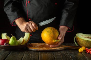 Olgun bir kavunu dilimlemeden önce mutfak masasında çalışma ortamı. Bıçak şefin elinde. Meyve diyeti konsepti. Asya mutfağı.