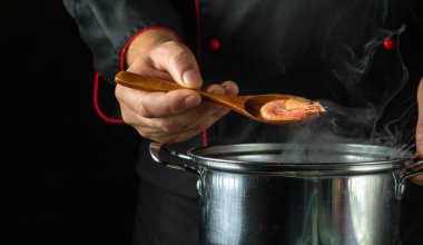 Şef mutfakta bir tavada lezzetli karides hazırlıyor. Restoran için lezzetli karides yemeği konsepti. Kaşık aşçının elinde karides.