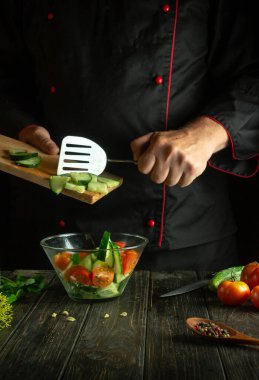 Profesyonel bir şef mutfakta sebze salatası hazırlar. Domatesli ve salatalıklı vitamin salatası pişirme kavramı. Siyah arkaplanda reçete için yer.