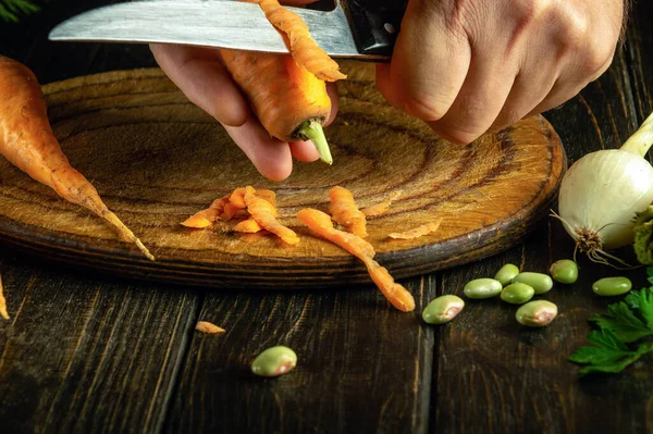 Cooking vegetable dishes from carrots and fresh vegetables. Close-up of a chef hands with a knife