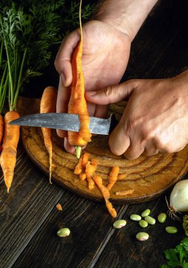 Bir aşçı, sebze yemeği hazırlamak için mutfak tahtasındaki bıçakla havuç soyardı. Vejetaryen gıda konsepti.
