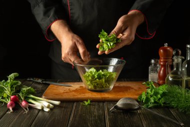 Aşçı sebze salatasıyla birlikte bir tabağa maydanoz koyar. Restoran mutfağında çalışma ortamı. Taze sebzeli lezzetli yemekler..