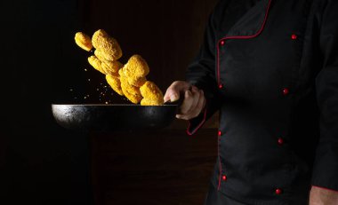 Şef sıcak tavada çıtır çıtır nagit hazırlıyor. Pişirme ellerindeki kızartma tavasının üzerinde uçan dırdırcılar. Siyah arkaplanda reçete için yer.