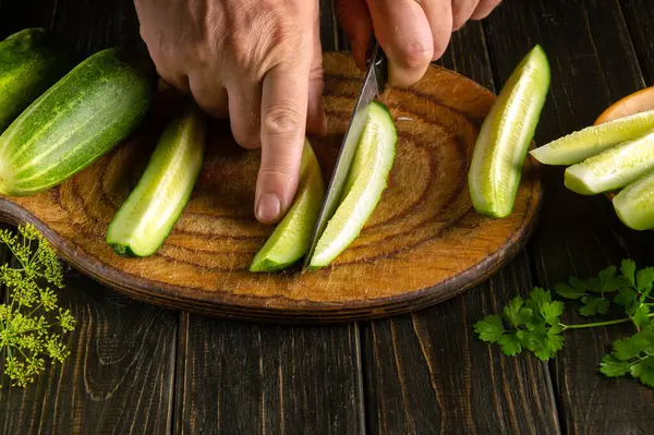 Slicing cucumbers with a knife in the hands of a chef before preparing a vegetable salad. Vegetarian diet concept
