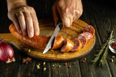 Bir şef ahşap kesme tahtasına bıçakla et sosisi kesiyor. Atıştırmak için lezzetli kahvaltı sandviçleri yapma kavramı.