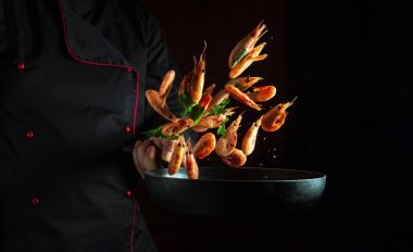 Profesyonel şef elinde donmuş karides ve maydanozlu bir tava tutuyor. Siyah bir arka planda izole edilmiş. Deniz ürünleri, deniz ürünleri tarifleri, restoran ve otel yemekleri..