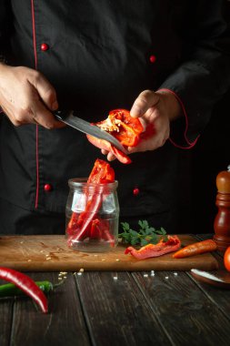 Kavanozda konserve dilimlemeden önce kapsülleri soymak. Bir restoranın mutfağında bir bıçak ve bir dilim dolma biberle şefin elleri.