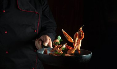 Bir şef bir restoran mutfağında karides hazırlar. Kızartma tavasının üzerinden bir şefin elinde karides uçuşu. Tarif veya menü için siyah boşluk.