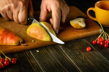 Aşçı komposto veya meyve suyu hazırlamak için bir kesme tahtasına olgun bir armut keser. Bir dizi vitamin için armut diyeti.