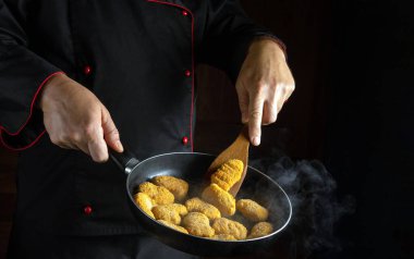 Şef kızartma tavasında çıtır çıtır nugget kızartıyor. Otel ya da restoran için lezzetli atıştırmalık konsepti. Siyah arkaplanda tarif veya menü için yer.