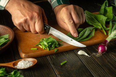 Erkek elleri, ıspanağı kesme tahtasının üzerinde bıçakla kesiyor. Evde vejetaryen yemeği pişirmek. Sebze diyeti fikri.