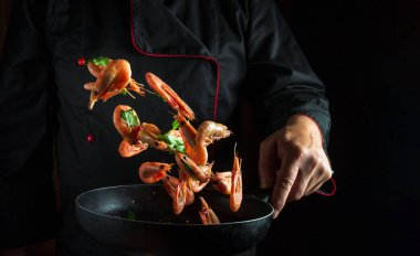 Profesyonel bir aşçı elinde donmuş karides ve maydanozla kızartma tavası tutar. Menü için siyah arkaplanda boşluk. Deniz ürünleri tarifleri veya bir restoranda veya otelde yemek pişirmek..