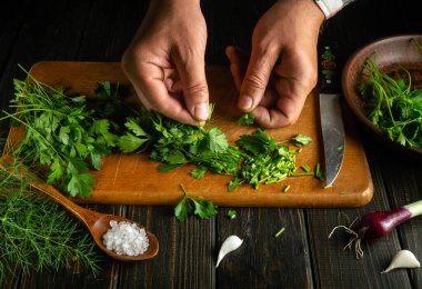 Şef taze sebzeli ve maydanozlu salata hazırlıyor. Evde, mutfak masasında vejetaryen yemeği pişirmek.