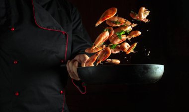 Aşçı kızartma tavasında karides pişirir. Tarif için siyah alan. Restoran mutfağında deniz ürünleri pişirme fikri...