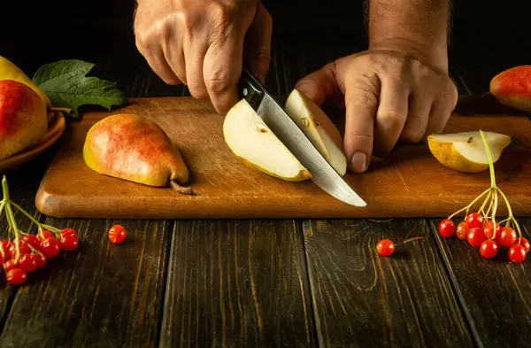 The cook\'s hands use a knife to cut pears on a wooden cutting board to prepare a delicious fruit drink. Pear diet idea. Copy space.