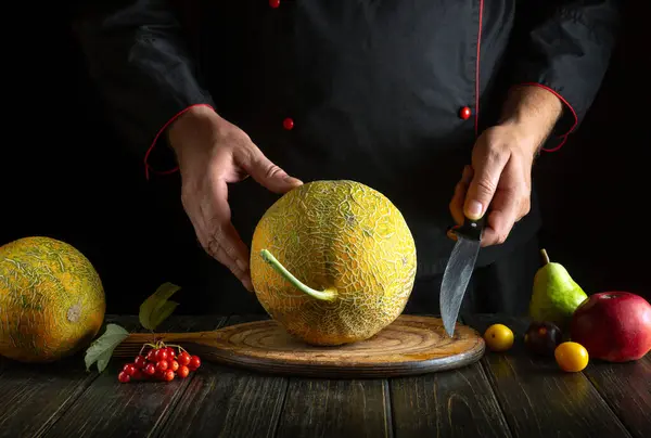 A knife in the hand of a chef for slicing a ripe melon on the kitchen table. Concept of serving dessert in a restaurant