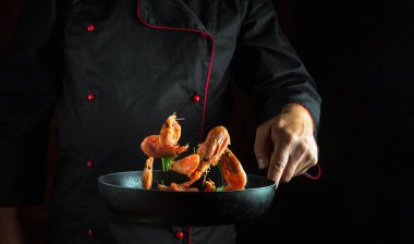 Tecrübeli şef karidesi otlu bir tavada pişirir. Deniz mahsulleri ve sağlıklı vejetaryen yiyecekler pişirme kavramı karanlık bir arka planda yemek tarifi ya da menü için yer vardır.