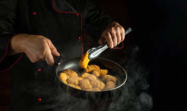 Şef kızartma tavasında tavuk nugget hazırlıyor. Restoranın ya da otelin mutfağında dırdır etme kavramı. Siyah arkaplanda reklam için boş alan