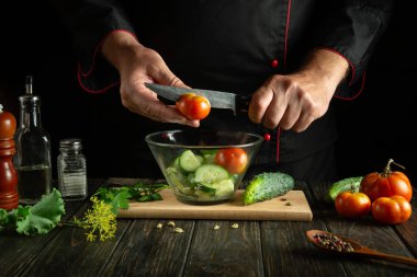 Aşçı mutfaktaki taze sebze salatasına domates ekler. Bıçak şefin elindeydi. Sağlıklı vejetaryen gıda konsepti