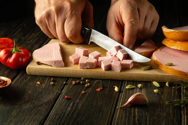 Slicing scalded sausage with a knife in the hands of a cook for preparing a delicious lunch on the kitchen table. Fast food concept.