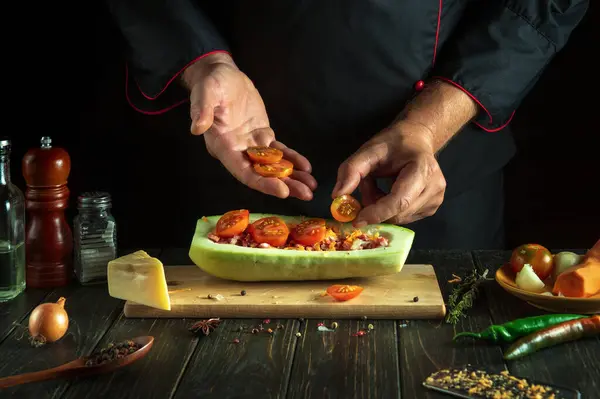 Professional chef adds a tomato to the zucchini. The concept of cooking a national stuffed squash boat or marrow in a restaurant or hotel kitchen.