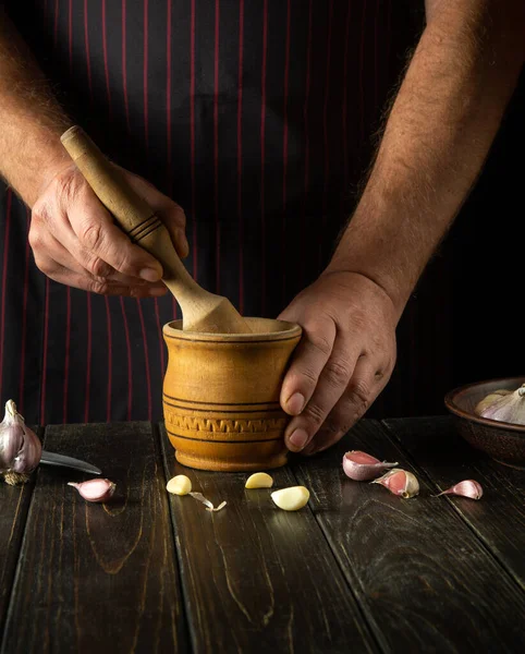 The chef crushes the garlic with a wooden pestle and mortar. We are preparing a national dish. Close-up of a chef\'s hands while working. Peasant products.