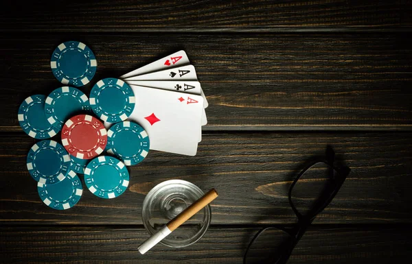 Popular poker game with a winning combination of four of a kind or quads. Cards with chips and and glasses with a cigarette on a vintage black table in a poker club