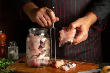 Bir aşçı kavanozu konserve ve tuzlama için balık biftekleriyle doldurur. Restoran mutfak masasında çalışma ortamı.