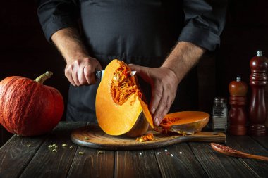 Bir şef mutfak mutfağında tahta bir tahtanın üzerinde mutfak bıçağıyla balkabağını keser. Mevsimlik güz yemeği, çorba ya da ulusal Amerikan turtası hazırlama süreci.