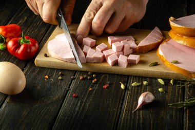 Lezzetli bir salata hazırlamak için bir şefin elinde bıçakla haşlanmış sosis dilimlemek. Tatil masasına yemek hazırlama kavramı.