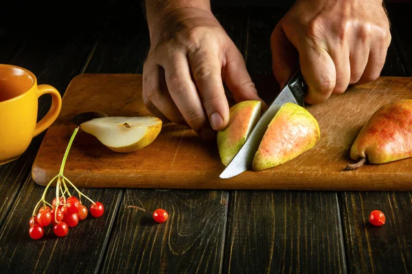A man hands cut a ripe pear with a knife on a cutting board to prepare compote or fruit juice. Sweet pears for a set of vitamins.