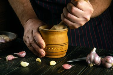 Mutfak masasında bir aşçının eliyle havanda sarımsak ezmek. Restoran mutfağında yemek pişirme kavramı.