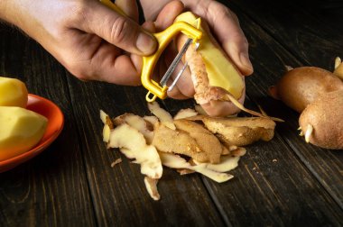 Aşçı patates kızartması ya da patates yemeği hazırlamak için patates soyar. Siyah bir masanın üzerinde, şefin elinin yakın plan çekimi için patates soyacağı kullanıyor..