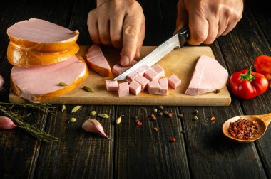 Bir adam kahvaltıya et yemeği hazırlamak için haşlanmış sosisi bıçakla küçük parçalara ayırır. Reklamcılık için karanlık alan