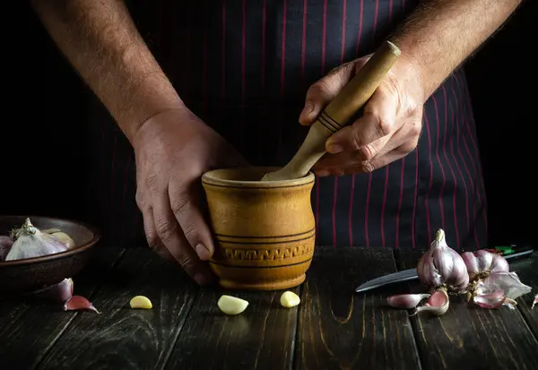 An experienced chef crushes garlic on the kitchen counter in a mortar before adding it to food. Close-up of a cook hands chopping garlic.
