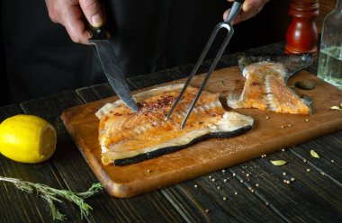 Aşçı mutfak masasında alabalık bifteği hazırlıyor. Pembe somon, akşam yemeği pişirmek için lezzetli bir balıktır. Restoran mutfağında baharatlı balık hazırlama süreci..