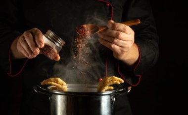 Pişirilmiş tavuk bacaklı bir tavaya elinde kaşıkla kuru aromatik baharatlar eklemek. Restoranın ya da otelin mutfağında lezzetli ve zengin bir çorba hazırlama fikri..
