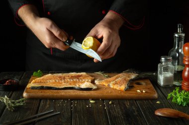 Mutfak masasında taze limonla alabalık bifteği tatlandıran bir şef. Pembe somon, akşam yemeği pişirmek için lezzetli bir balıktır. Restoran mutfağında balık hazırlama süreci..
