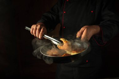 Un hamurundan krep kızartırken mutfakta bir aşçının ellerinde maşa ve kızartma tavası var. Reklam için siyah alan.