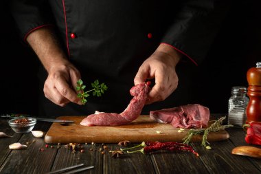 Mutfak masasında, aromatik baharatlar ve maydanozlu bir şefin elleriyle biftek hazırlama süreci. Akşam yemeği için sulu ve aromatik bir barbekü pişiriyorum.