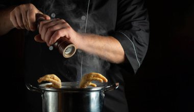 Şef kaynamış tavuk budu tenceresine kuru biber ekler. Restoran mutfağında lezzetli ve zengin çorba hazırlama fikri. Reklam için siyah alan