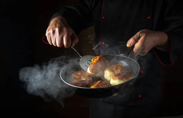 The chef is preparing oladki in a frying pan. The concept of preparing Ukrainian national dish or bliny in the kitchen. Black space for recipe or menu.