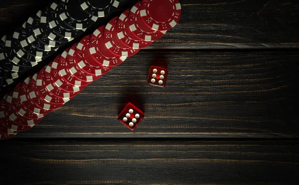 Craps or dice game on a dark vintage wooden table in a club. Red and black chips from a lucky win. Free dark space for advertising. Luck in gambling.
