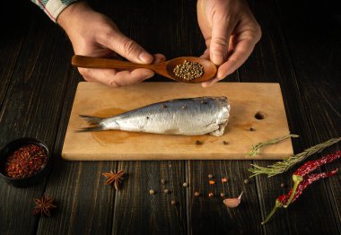 Şef lezzetli bir akşam yemeği için mutfak masasında baharat ve kişniş ile Clupea balığı hazırlıyor. Mutfak masasında çalışma ortamı.